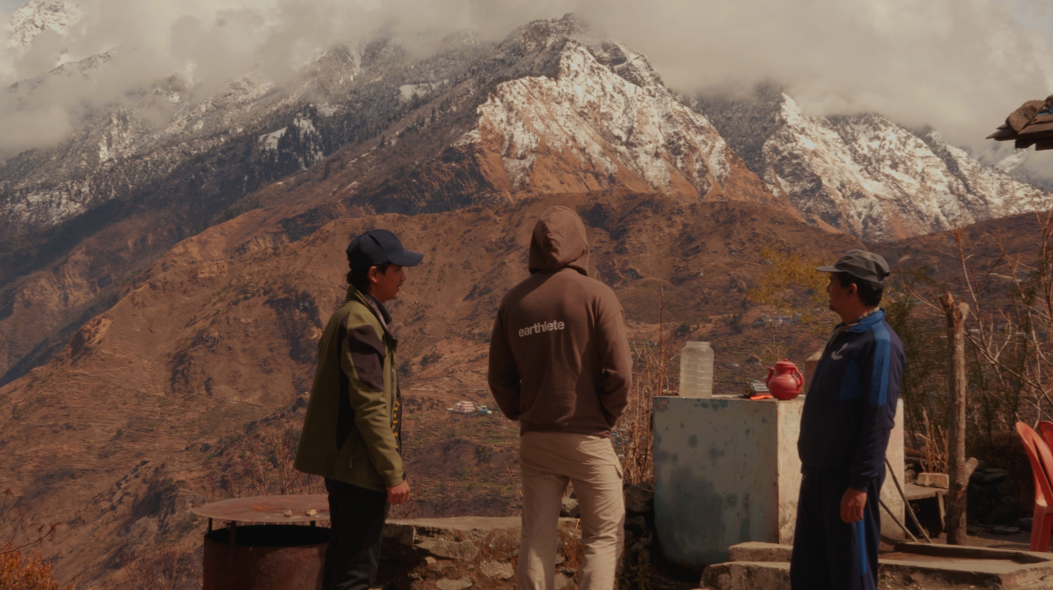 Three people standing in a mountainous area with snow-capped peaks.