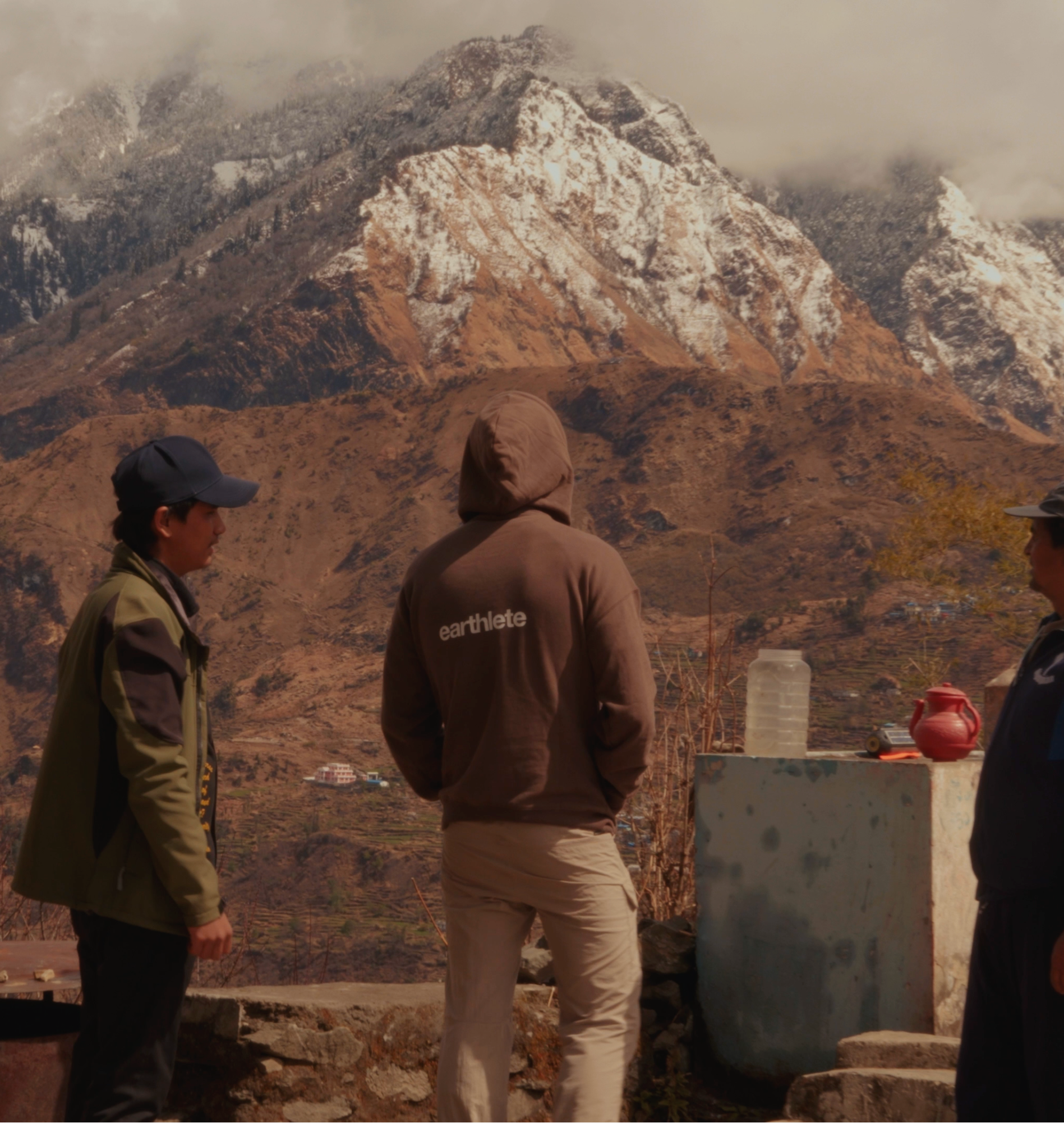 Three people standing in a mountainous area with snow-capped peaks.