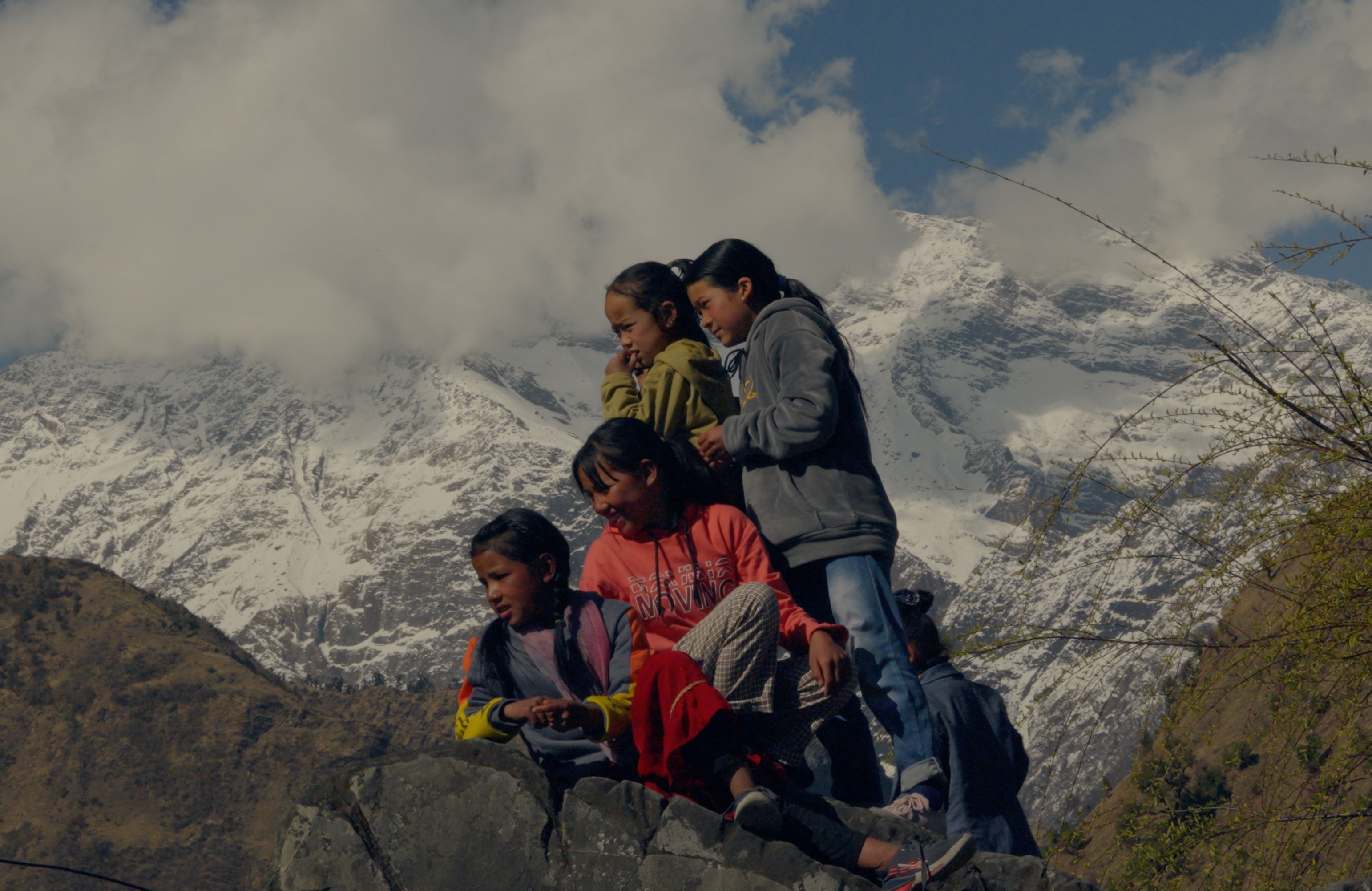 Four people sitting on a rock with snow-capped mountains in the background
